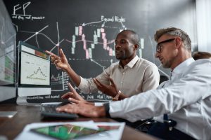 Two colleagues analysing the stock market on the Trades Trek free stock simulator, while sitting down